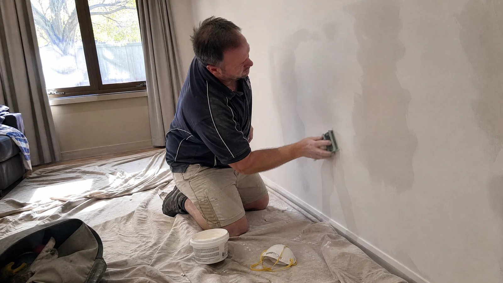 Handyman sanding back a patched plasterboard wall in a Canberra home
