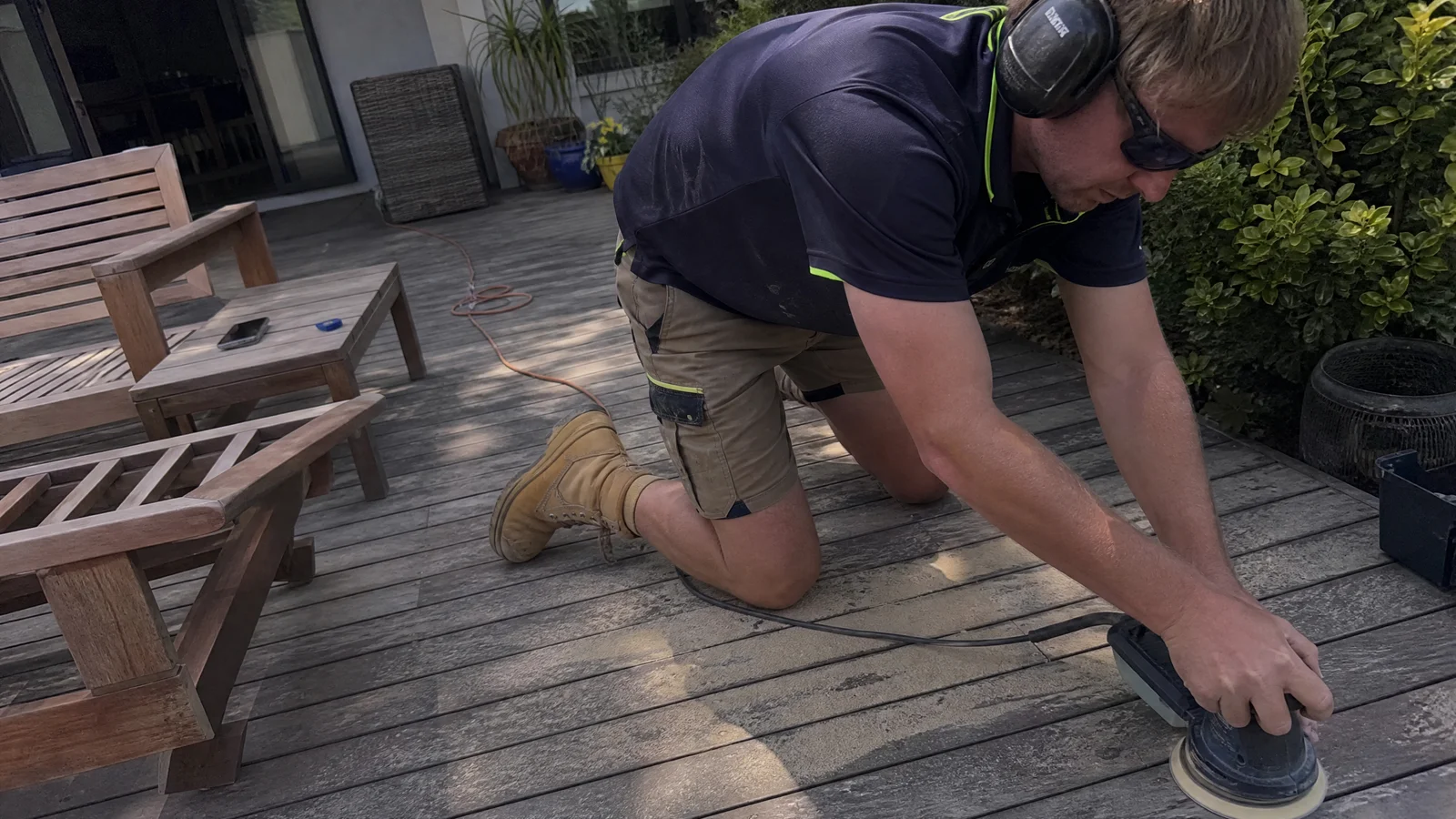 Tradesman sanding back weathered merbau decking in a Canberra backyard