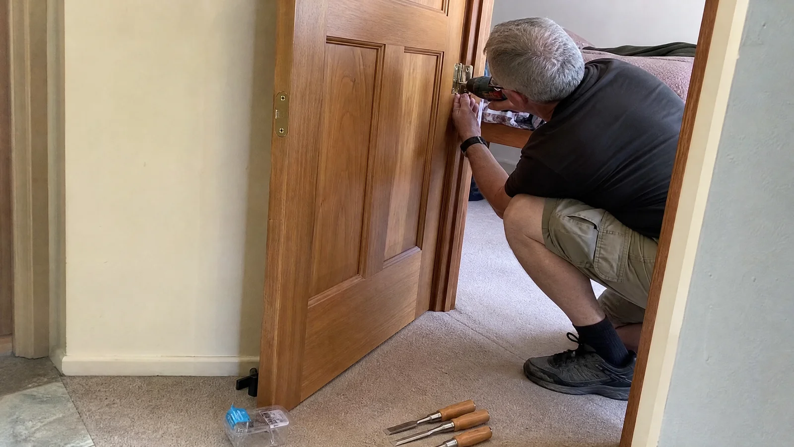 Handyman adjusting a hinge on an internal timber door in a Canberra hallway